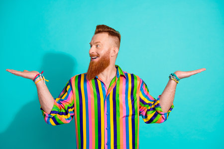Photo of looking left side redhair bearded businessman in striped shirt holding balance two arms isolated on aquamarine color backgroundの写真素材