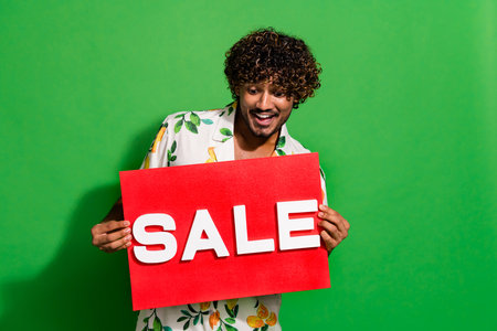 Photo portrait of handsome young guy hold look sale plate shopping dressed stylish citrus print garment isolated on green color backgroundの写真素材