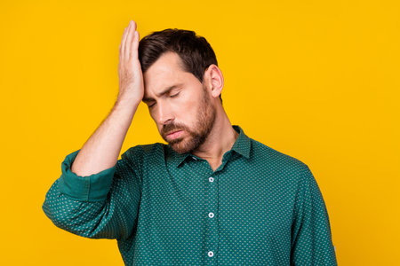 Photo of tired overwhelmed man with stylish haircut dressed dotted shirt have headache feel bad isolated on yellow color backgroundの写真素材