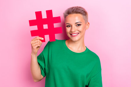 Photo of cheerful adorable woman popular blogger wear green trendy clothes sowing hashtag isolated on pink color backgroundの写真素材