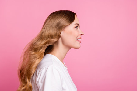 Side profile photo of gorgeous girl with fluttering hair dressed white t-shirt look at promo empty space isolated on pink color backgroundの写真素材