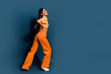 Full body photo of beautiful sportive figure lady showing her butt trying new orange pants  isolated on dark blue color backgroundの写真素材