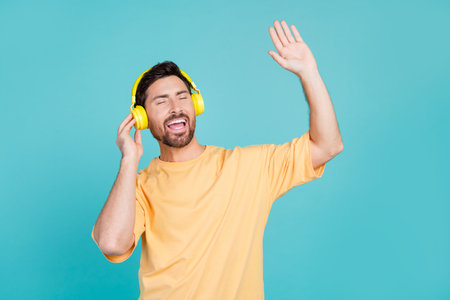 Photo of young guy positive moves party after hard week singing songs listening headphones raised hand up isolated on cyan color backgroundの写真素材