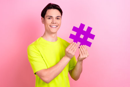 Photo portrait of nice teen man hold hashtag influencer dressed stylish yellow clothes isolated on pink color backgroundの写真素材