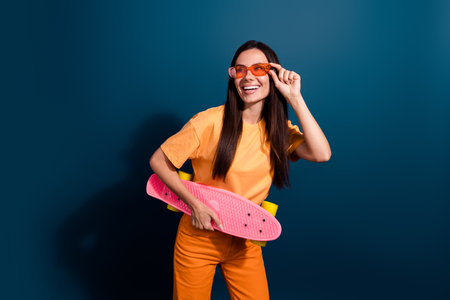 Photo of woman touching orange sunglasses had hobby ride skateboard looking empty space activities isolated on dark blue color backgroundの写真素材