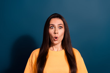 Photo of speechless woman with long hairstyle dressed yellow t-shirt staing at impressive discount isolated on dark blue color backgroundの写真素材
