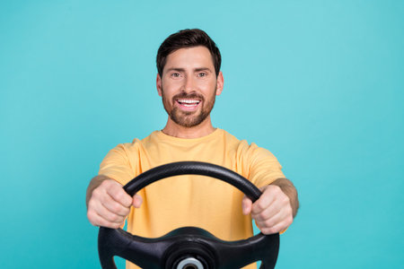 Photo of happy brunet hair man holding steering wheel his first automobile  with good price isolated on aquamarine color backgroundの写真素材