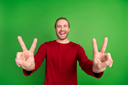 Photo of optimistic funky man with stubble long hairdo dressed red pullover two hands showing you okey isolated on green color backgroundの写真素材