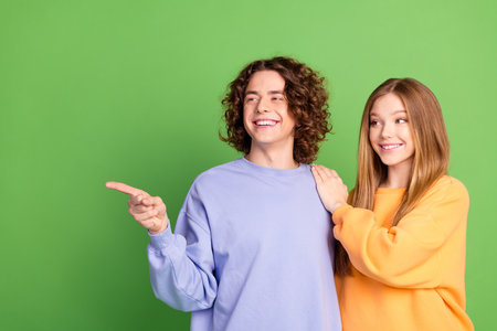 Portrait of positive nice people cuddle look direct finger empty space proposition isolated on green color backgroundの写真素材