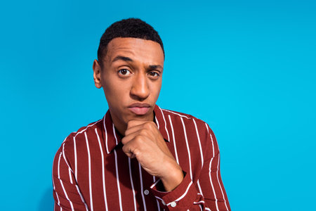 Photo portrait of pretty young male raise eyebrow suspicious look dressed stylish striped outfit isolated on blue color backgroundの写真素材