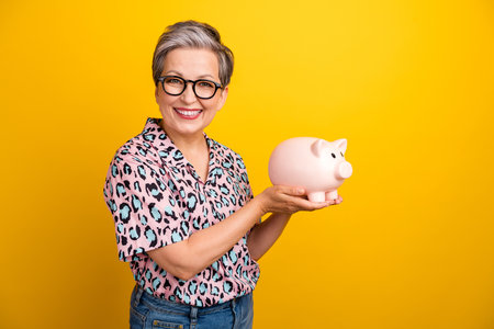 Photo portrait of attractive pensioner woman hold piggy savings wear trendy leopard print clothes isolated on yellow color backgroundの写真素材