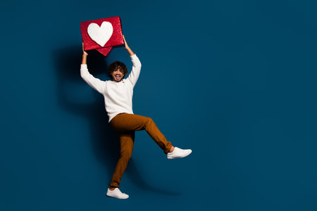 Full length photo of positive good mood man wear white sweater rising heart like sign walking empty space isolated dark blue color backgroundの写真素材