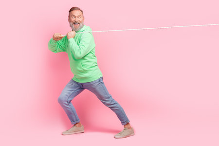 Full length photo of handsome senior man pulling string turn around wear trendy green garment isolated on pink color backgroundの写真素材