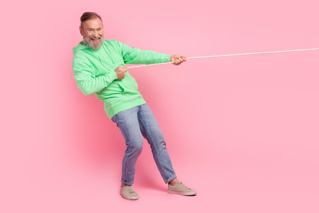 Full size photo of cool pensioner man pulling string strength wear trendy green clothes isolated on pink color backgroundの写真素材