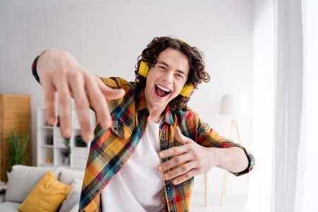 Photo of funky cool guy dressed checkered shirt dancing listening music headphones indoors house...