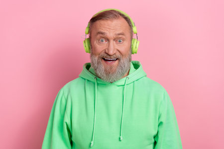 Photo of excited funky guy dressed green hoodie listening songs headphones isolated pink color backgroundの写真素材