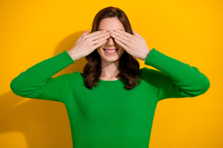 Photo of cheerful carefree girl wear stylish green clothes two arms cover eyes isolated on yellow color backgroundの写真素材