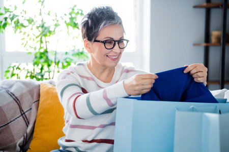 Portrait of cheerful grandmother sitting sofa enjoy open shop order bags free time apartment indoorsの写真素材