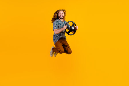 Full length photo of impressed excited guy wear print shirt jumping high riding car isolated yellow...
