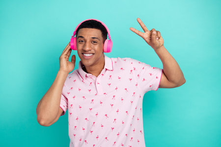 Portrait of nice positive man beaming smile arm touch headphones demonstrate v-sign isolated on turquoise color backgroundの写真素材