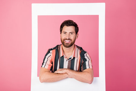 Photo of handsome man with bristle folded hands inside paper frame shooting his white teeth smile...