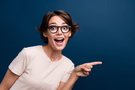 Photo portrait of lovely young lady point excited empty space dressed white garment isolated on dark blue color backgroundの写真素材