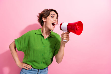 Photo portrait of attractive young woman hold shout megaphone empty space dressed stylish green clothes isolated on pink color backgroundの写真素材