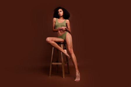 No filter photo of gorgeous woman wearing comfort activewear sitting stool posing empty space isolated on brown color backgroundの写真素材
