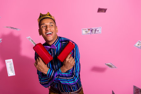 Photo of funky cheerful guy wear striped shirt golden crown shooting money gun isolated pink color...