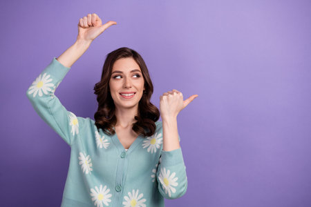Photo of cheerful dreamy woman wear flower print cardigan looking pointing two thumbs empty space isolated purple color backgroundの写真素材