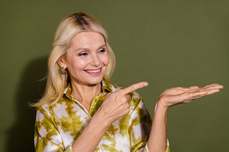 Photo of cheerful satisfied charming lady demonstrate empty space recommend buy product isolated on khaki color backgroundの写真素材