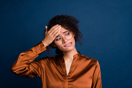 Photo of uncertain nervous lady wear silk brown shirt spectacles arm head biting finger looking empty space isolated blue color backgroundの写真素材