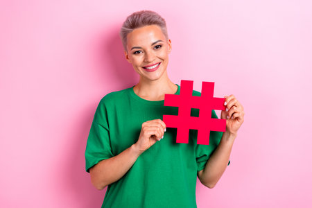 Photo of positive lovely cute woman wear green clothes demonstrate paper card hashtag isolated on...