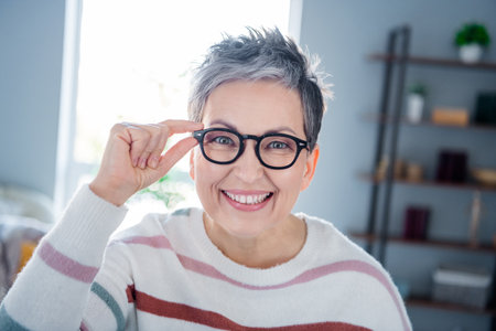 Photo of sweet adorable woman dressed striped sweater arm hand eyewear smiling indoors house home roomの写真素材