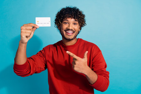 Photo of happy indian student received premium card for shopping purchases point finger plastic isolated on aquamarine color backgroundの写真素材