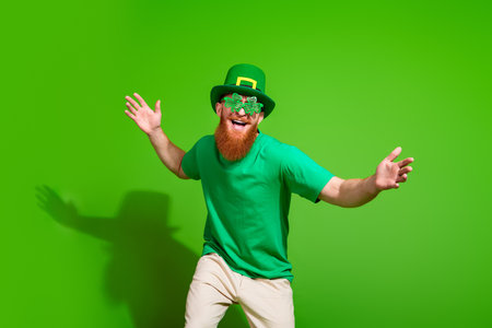 Portrait of charismatic cheerful irish man shamrock shape glasses dancing clubbing isolated on green color backgroundの写真素材