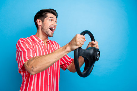 Photo of impressed funky guy wear red shirt riding car looking empty space isolated blue color backgroundの写真素材