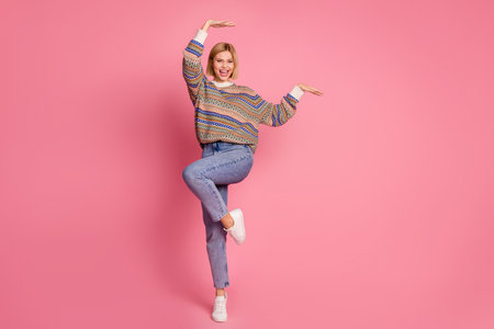 Full length photo of gorgeous woman dressed print sweater denim pants dancing raising hands up have...