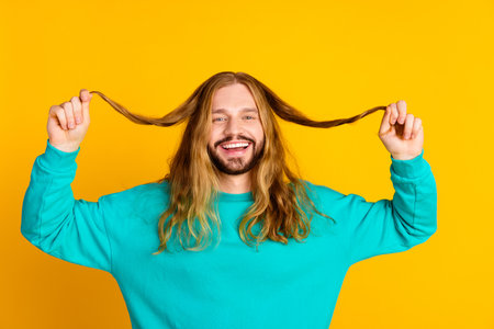 Photo of excited nice person toothy smile hands hold long hairstyle ends isolated on yellow color backgroundの写真素材