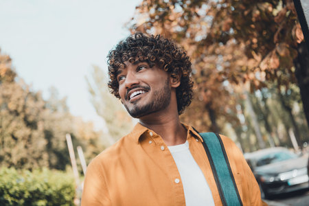 Portrait of positive hispanic man student walking in park looking city urban landscape sunny day...