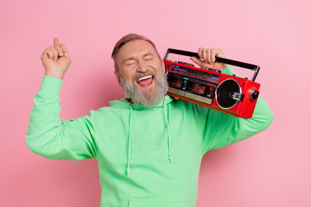 Photo of excited carefree man wear green sweatshirt singing listening boom box songs isolated pink...