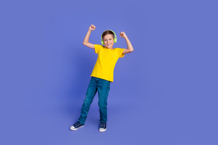 Photo of cheerful crazy good mood boy wear stylish yellow clothes raise hands fists listen music isolated on purple color backgroundの写真素材
