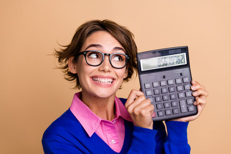 Photo portrait of pretty young girl look excited calculator wear trendy blue outfit isolated on beige color backgroundの写真素材