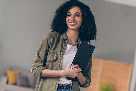 Portrait of pretty young woman contemplate hold pen clipboard wear khaki shirt modern interior house indoorsの写真素材
