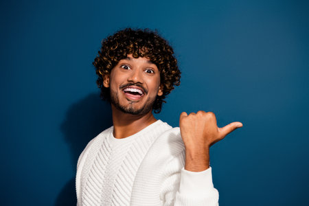 Photo of funky impressed man wear white sweater pointing thumb empty space isolated dark blue color...
