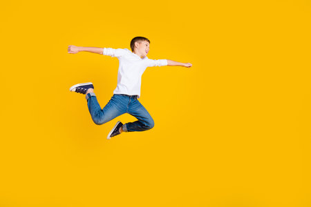 Full length photo of funky carefree boy wear white shirt jumping high flying empty space isolated yellow color backgroundの写真素材