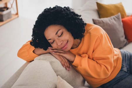 Photo portrait of lovely young lady closed eyes lean on sofa sleepy dressed casual orange clothes cozy day light home interior living roomの写真素材