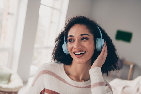 Photo of cheerful dreamy lady dressed striped pullover listening music headphones indoors apartment roomの写真素材