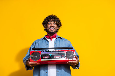 Photo portrait of handsome young guy hold excited boombox dressed stylish jeans garment red scarf isolated on yellow color backgroundの写真素材