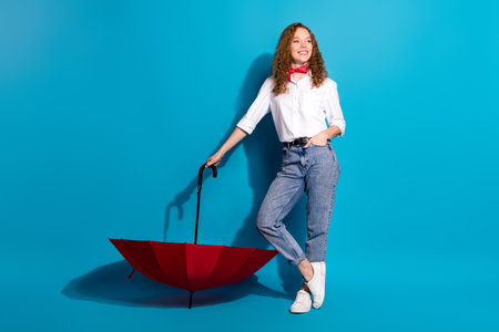 Photo portrait of pretty young woman hold umbrella look empty space dressed stylish white clothes isolated on blue color backgroundの写真素材
